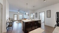 Located in Boerne, Texas, this single-story, 2-bedroom, 2-bathroom residence offers a thoughtfully designed open-concept floor plan that maximizes functionality and comfort. The kitchen serves as a central hub of the home, showcasing rich dark cabinetry, granite countertops, a large center island with a built-in sink and seating, pendant lighting, track lighting, and black appliances — all flowing seamlessly into the living and dining areas. The living room features wood-look hard flooring, a ceiling fan, and natural light from large windows. Both bedrooms are carpeted and include ceiling fans, with the generously sized primary bedroom offering direct access to its en-suite bathroom. The primary bathroom features dark cabinetry with granite countertops and a tub-shower combo with tile surround. A spacious walk-in closet with wire shelving provides ample storage. The second bathroom mirrors the same refined finishes, including a granite vanity and tub-shower combination. Two closets throughout the home add further storage convenience. The overall aesthetic is clean and modern, with a neutral color palette and consistent finishes creating a cohesive, move-in-ready atmosphere.