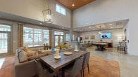 Located at 230 Pine Knot Ln in Graham, NC, this single-floor community clubhouse is designed to impress with its open-concept layout and dramatic soaring ceilings accented by a warm terracotta-toned vaulted detail. Polished concrete floors flow seamlessly throughout the expansive space, lending a modern, sophisticated aesthetic that ties all areas together.

The main lounge area is generously appointed with large sectional sofas, accent chairs, and area rugs, creating a welcoming environment for relaxation and socializing. A rustic wood dining table with contemporary chairs provides an inviting gathering spot, complemented by elegant geometric pendant lighting overhead.

Adjacent to the lounge, a well-equipped kitchenette features dark cabinetry, granite countertops, a built-in microwave, and a coffee bar station — ideal for entertaining and community events. Wall-mounted televisions are thoughtfully positioned throughout the space for convenience.

A dedicated recreation area houses a full-size billiards table beneath warm pendant lighting, adding a fun and engaging element to the clubhouse experience. Decorative artwork, including vibrant botanical canvas pieces, adds color and character throughout.

Large windows and glass double doors flood the interior with natural light and offer views of the outdoor community spaces beyond, creating a seamless indoor-outdoor connection. The overall ambiance is modern, comfortable, and purposefully designed for community living.