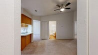 This single-floor residence offers a practical and well-organized layout across several distinct areas. The main living space is carpeted in neutral tones and features a ceiling fan with integrated lighting, creating a comfortable and functional environment. A sliding glass door allows natural light to filter in and provides views of the surrounding greenery, enhancing the room's open feel.

The kitchen is equipped with warm-toned oak cabinetry providing ample storage, light-toned countertops, a stainless steel sink, and white appliances including an electric range and dishwasher. Natural light enters through a window fitted with vertical blinds. The kitchen connects conveniently to the main living area via a pass-through counter arrangement.

The bedrooms are carpeted and finished with neutral walls, each featuring windows with vertical blinds that allow for natural light. One bedroom includes direct access to the bathroom, which contains a walk-in shower enclosed by a chrome-framed glass door with white tile surround.

A dedicated laundry area houses a full-size top-load washer and dryer side by side beneath a utility shelf, with durable hardwood-style flooring underfoot. Throughout the space, a consistent neutral color palette and clean finishes contribute to a simple, move-in-ready ambiance.