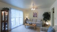 This single-floor residence offers a comfortable and well-lit layout designed for everyday living. The living room serves as the centerpiece of the space, featuring large sliding glass doors dressed with vertical blinds that allow generous amounts of natural light to fill the room while providing access to an outdoor area. The ceiling is finished with a textured surface and fitted with a ceiling fan with integrated lighting, ensuring year-round comfort and ambiance. Soft wall-to-wall carpeting runs throughout, adding warmth underfoot and contributing to the room's inviting atmosphere. The neutral wall tones create a versatile backdrop that complements a range of furnishing styles. The overall ambiance is calm and approachable, with a layout that makes efficient use of the available space. The combination of natural light, functional ceiling features, and soft flooring gives this residence a cozy yet practical character well-suited for comfortable day-to-day living.