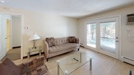 This single-floor residence offers two bedrooms and two full bathrooms within a thoughtfully organized layout. The living area features light tile flooring, a neutral color palette, and French doors that invite natural light and provide outdoor views, creating a bright and welcoming atmosphere. Seating is arranged around a glass coffee table, lending the space an open, airy feel.

The kitchen is equipped with stainless steel appliances, including a range, microwave, refrigerator, and dishwasher. White cabinetry pairs with dark granite-style countertops, and the kitchen opens toward the main living area via a peninsula layout with light wood-style flooring throughout.

Both bedrooms are carpeted and feature neutral tones. One bedroom accommodates two beds, a nightstand with lamp, and benefits from multiple windows that bring in natural light. A dark wood dresser with mirror and a walk-in closet provide ample storage. The second bedroom also fits two beds, a nightstand, and includes a mirrored closet.

Each bathroom is finished with tile flooring, a white vanity, and a tub-shower combination, maintaining a clean, functional aesthetic throughout.