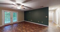 This single-story residence features three bedrooms and two full bathrooms within a spacious, well-appointed layout. Rich, dark hardwood-style flooring runs throughout the main living areas, complementing bold deep green accent walls that lend a distinctive character to the space. The living area is generously sized, featuring a ceiling fan with light fixture, a textured ceiling, and a sliding glass door that opens to an outdoor deck, allowing natural light to filter in and providing views of surrounding greenery.

The open-concept design connects the living area to the kitchen, which is equipped with dark espresso-toned cabinetry, white countertops, a stainless steel sink, and black appliances including a range and microwave. Stainless steel appliances, including a refrigerator, are also visible from the adjoining space.

Each bedroom features plush carpeting, a ceiling fan, and windows that bring in natural light. Accent walls in deep green and navy blue add visual interest and personality to individual rooms. The two bathrooms are finished with wood-grain cabinetry, white countertops, hardwood-style flooring, and tub-shower combinations, offering a clean and modern aesthetic throughout.
