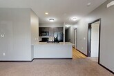 Located at 15707 Grand Plaza in Omaha, Nebraska, this two-story unit offers a well-organized layout spread across two levels. The lower level houses an attached garage with concrete flooring and an automatic opener, along with a tiled entry corridor and staircase leading to the main living area above.

The upper level comprises the majority of the living space and features an open-concept design that seamlessly integrates the living room, dining area, and kitchen. The living room is carpeted and benefits from natural light through large windows and a sliding door that opens to a balcony, complemented by a ceiling fan overhead. The kitchen is well-appointed with dark cabinetry, black appliances including a refrigerator with ice maker, electric range, and microwave, along with a granite-topped peninsula with an undermount sink — ideal for both cooking and casual dining.

The bedroom is a comfortable, carpeted space with natural light from a window and its own ceiling fan. Three closets throughout the unit provide generous storage, with one featuring built-in wire shelving systems for organized storage. The bathroom includes a dark-stained vanity with granite countertop, tile flooring, and a clean, functional layout. Neutral gray tones and dark trim carry throughout, giving the space a cohesive, modern aesthetic.