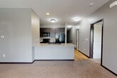 Located at 15707 Grand Plaza in Omaha, Nebraska, this two-story unit offers a well-organized layout spread across two levels. The lower level houses an attached garage with concrete flooring and an automatic opener, along with a tiled entry corridor and staircase leading to the main living area above.

The upper level comprises the majority of the living space and features an open-concept design that seamlessly integrates the living room, dining area, and kitchen. The living room is carpeted and benefits from natural light through large windows and a sliding door that opens to a balcony, complemented by a ceiling fan overhead. The kitchen is well-appointed with dark cabinetry, black appliances including a refrigerator with ice maker, electric range, and microwave, along with a granite-topped peninsula with an undermount sink — ideal for both cooking and casual dining.

The bedroom is a comfortable, carpeted space with natural light from a window and its own ceiling fan. Three closets throughout the unit provide generous storage, with one featuring built-in wire shelving systems for organized storage. The bathroom includes a dark-stained vanity with granite countertop, tile flooring, and a clean, functional layout. Neutral gray tones and dark trim carry throughout, giving the space a cohesive, modern aesthetic.