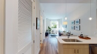 This well-appointed single-floor residence offers a cohesive, contemporary design defined by clean lines, neutral tones, and abundant natural light. The open-concept layout connects the kitchen and living area seamlessly, creating a spacious and functional flow. The kitchen is outfitted with light wood cabinetry extending to the ceiling, a tiled backsplash, stainless steel appliances including a refrigerator, range, microwave, and dishwasher, and a peninsula with a quartz countertop and undermount sink. Pendant lighting above the peninsula adds a refined touch. Wood-look flooring runs throughout the main living areas, complementing the bright, airy palette.

The living room receives generous natural light through large windows framing lush outdoor greenery, creating a calm and welcoming atmosphere. A louvered storage feature near the entry adds practical character to the entryway corridor.

The primary bedroom opens directly to a private balcony through floor-to-ceiling sliding glass doors, offering outdoor access and verdant views. The secondary bedroom features carpeted flooring and a walk-in closet. Both rooms are well-proportioned with ample storage.

The bathroom is finished with marble-style tiled walls surrounding the tub-shower combination, warm wood cabinetry, and a quartz vanity countertop, maintaining the residence's cohesive, modern aesthetic.