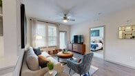 This single-floor residence offers a thoughtfully designed layout that balances comfort and contemporary style. The living room serves as the heart of the home, featuring wood-look plank flooring, a ceiling fan with light fixture, and multiple windows fitted with blinds and sheer curtains that invite generous natural light. The space comfortably accommodates a sofa, accent chairs, a round ottoman coffee table, and a media console, creating a warm and functional gathering area.

The kitchen is outfitted with grey cabinetry, granite countertops, stainless steel appliances including a French door refrigerator, a subway tile backsplash, and pendant lighting. An island with additional counter space adds versatility for meal preparation.

Two bedrooms provide restful retreats. One features a blue accent wall and large windows with garden views, while the other is accented with warm-toned artwork and rich upholstered furnishings. Both rooms offer ample natural light.

The two bathrooms maintain a consistent design language, featuring wood-look flooring, granite vanity tops, and grey cabinetry. One includes a full soaking tub with large-format tile surround, while the other offers an elongated vanity with a well-lit mirror. The overall ambiance is modern, cohesive, and residential.