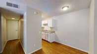 This single-floor residence offers a practical and comfortable layout with consistent finishes throughout. The living area is spacious and bright, featuring warm wood-look laminate flooring and a textured ceiling. A full-length sliding glass door fitted with vertical blinds fills the room with natural light and provides direct access to an outdoor area, offering views of the surrounding landscape.

The kitchen is efficiently designed with white cabinetry above and below the counter, a double-basin stainless steel sink, granite-style laminate countertops, and black appliances including a range and dishwasher. The wood-look flooring continues seamlessly from the living area into the kitchen, creating a cohesive flow.

A narrow hallway connects the main living spaces to the private areas of the unit, with recessed lighting overhead and consistent wood-look flooring underfoot. The bedroom features plush carpeting, neutral-toned walls, a textured ceiling, and a double-door closet providing ample storage.

The bathroom is clean and functional, equipped with a single-sink vanity topped with a granite-style surface, a full-size soaking tub and shower combination with a curved curtain rod, and wood-look flooring. Together, these spaces create a cohesive, low-maintenance living environment suited for everyday comfort.