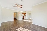 This single-floor residence offers a clean, functional layout with consistent hardwood-style flooring flowing throughout the space, creating a cohesive and polished look from room to room. The living area is a standout feature, highlighted by elegant crown molding, a ceiling fan with a light fixture, and a set of French doors that invite natural light and provide outdoor access. An additional window further brightens the room, contributing to an open and airy atmosphere. The kitchen is designed for practicality, featuring rich warm-toned cabinetry, granite-style countertops, a double sink, and white appliances including a range, refrigerator, and overhead microwave. A closet door within the kitchen provides convenient pantry or storage space. The bathroom is accessible via a hallway flanked by closets, offering ample built-in storage. The vanity area features white cabinetry, a large mirror, and a well-lit fixture above. A separate wet area includes a full soaking tub surrounded by classic white tile. The bedrooms are comfortably sized with neutral walls, hardwood-style flooring, and windows fitted with blinds that allow for natural light and privacy. Overall, the space presents a tidy, move-in-ready environment with practical finishes and a welcoming ambiance throughout.