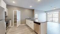This single-floor unit presents a clean, modern aesthetic enhanced by neutral warm-gray wall tones and light wood-look flooring that flows throughout the main living areas. The kitchen serves as a central feature, equipped with white shaker-style cabinetry, granite-look countertops, and a full suite of stainless steel appliances including a refrigerator, range, microwave, and dishwasher. A peninsula provides additional counter space and casual seating potential, while recessed lighting illuminates the area effectively. A dedicated pantry with built-in shelving adds practical storage directly off the kitchen.

The bedrooms are carpeted for comfort and each features windows that bring in natural light and exterior views of the surrounding area. One bedroom benefits from a generously sized walk-in closet outfitted with wire shelving and hanging rods across multiple walls. The bathroom is finished with wood-look tile flooring, a white vanity with an integrated sink, a framed mirror, and a soaking tub with a shower surround. Throughout the unit, consistent use of brushed nickel hardware and white trim details contributes to a cohesive, well-maintained interior environment.