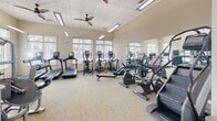 Located at 200 Greenfield Ln in Rockingham, Virginia, this single-floor fitness center is designed to support a comprehensive range of workout activities. The facility is divided into distinct functional zones, each thoughtfully outfitted for a specific type of training.

The cardio area is generously sized, housing multiple treadmills, elliptical trainers, and stationary bikes, including recumbent models. Large windows with slatted blinds line the walls, allowing abundant natural light to fill the space. Ceiling fans overhead aid in air circulation, while a drop-tile ceiling with recessed fluorescent lighting ensures consistent illumination throughout.

A dedicated strength training section features a full rack of dumbbells, weight benches, cable machines, a stair climber, and additional resistance equipment. A wall-mounted flat-screen television is positioned for convenient viewing, and a water station provides easy access for hydration. Floor-to-ceiling mirrors expand the sense of space and allow users to monitor their form.

Separate from the main gym floor is a studio room with soaring ceilings, warm hardwood flooring, and expansive mirrors spanning an entire wall. This versatile space is equipped with stability balls, yoga mats, and a mounted display screen, making it well-suited for yoga, stretching, or guided fitness classes.