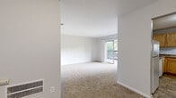 Located at 117 S Comanche Ct in Virginia Beach, VA, this single-floor unit offers a straightforward, functional layout designed for comfortable everyday living. The living area is spacious and bright, featuring neutral-toned carpet and a sliding glass door that opens to a private balcony, offering views of surrounding greenery. The open feel of the room is enhanced by clean white walls and ample natural light.

The bedrooms continue the carpeted aesthetic and maintain the neutral color palette throughout. Each room is well-proportioned, with one bedroom featuring a walk-in closet equipped with a built-in rod and shelving, while an additional bedroom includes a standard reach-in closet for convenient storage. Ceiling-mounted HVAC vents are present throughout, ensuring climate control in each space.

The bathroom is finished with tile flooring in a stone-like pattern and includes a full tub and shower combination with tiled surround, a white vanity with integrated sink, and chrome fixtures. The kitchen is outfitted with warm wood cabinetry, dark laminate countertops, a gas range with overhead ventilation hood, and matching tile flooring, providing a practical and well-equipped cooking space.