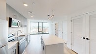 Located on the fifth floor at 801 N Orange Street in Wilmington, Delaware, this modern 2-bedroom, 2-bathroom unit offers a thoughtfully designed open layout with contemporary finishes throughout. Light wood-tone flooring runs seamlessly across the entire space, complementing the crisp white walls and clean architectural lines.

The combined kitchen and living area serves as the heart of the unit. The kitchen is outfitted with gray flat-front cabinetry, stainless steel appliances including a refrigerator, range, microwave, and dishwasher, and a white quartz-topped island that doubles as a casual dining and prep space. The living area is anchored by dramatic floor-to-ceiling windows with black metal frames, flooding the space with natural light and offering elevated views of the Wilmington cityscape.

Both bedrooms are bright and well-proportioned, with the primary bedroom featuring a large window overlooking the urban skyline. The bedrooms benefit from access to a dedicated closet for storage. The two bathrooms are finished with large-format tile flooring, light wood vanities with white countertops, and marble-surround tub and shower enclosures that add a refined, upscale touch. The overall ambiance of this unit is sleek, modern, and light-filled, ideal for urban living in the heart of Wilmington.