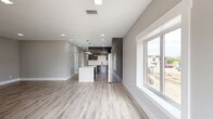 This single-floor residence offers a well-designed layout comprising two bedrooms, three bathrooms, and a combined kitchen and living area connected by two hallways. The open-concept living and kitchen area is immediately striking, featuring light-toned luxury vinyl plank flooring, recessed lighting, and large windows that flood the space with natural light while providing outdoor views of the surrounding neighborhood.

The kitchen is appointed with high-gloss dark wood-grain cabinetry reaching toward the ceiling, a white quartz waterfall island, subway tile backsplash, stainless steel appliances, and pendant lighting — delivering a sleek, contemporary aesthetic. The cabinetry extends to a full-height panel that serves as an architectural accent between the kitchen and living areas.

The bedrooms are finished with the same light-toned flooring and neutral grey walls, with windows offering exterior views. The generously sized primary bedroom provides ample space for furnishings.

The bathrooms showcase a refined design highlighted by large-format white marble-look porcelain tile flooring, floating dark vanities with white countertops, illuminated mirrors, and natural light from well-positioned windows. A utility area with marble-look tile flooring provides convenient access to mechanical systems and laundry connections.