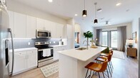 This well-appointed 2-bedroom, 2-bathroom residence offers a thoughtfully designed single-level layout that maximizes functionality and style. The open-concept kitchen and living area serves as the heart of the home, featuring crisp white cabinetry, a gray subway tile backsplash, stainless steel appliances — including a French door refrigerator — and a large center island with a quartz countertop and seating for multiple guests, illuminated by sleek pendant lighting. Light wood-tone flooring flows throughout the common areas, adding warmth to the bright, neutral color palette. The living room is filled with natural light from floor-to-ceiling sliding glass doors that open to an outdoor balcony. In-unit washer and dryer hookups offer added convenience. The primary bedroom features a distinctive accent wall, plush carpeting, and direct access to an en-suite bathroom with a dual-sink vanity topped with granite counters and a frameless glass walk-in shower with marble-style tile. A generously sized walk-in closet with built-in shelving and rod systems completes the primary suite. The second bedroom is bright and comfortable, with natural light from exterior windows and soft carpeted flooring. A second full bathroom serves the additional bedroom and guests.