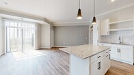 This thoughtfully designed 2-bedroom, 2-bathroom residence offers a cohesive, modern aesthetic throughout its single-floor layout. The open-concept kitchen and living area serves as the heart of the home, where warm hardwood-style flooring, crown molding, and neutral gray walls create a clean, inviting atmosphere. The kitchen is a standout feature, showcasing white shaker cabinetry with matte black hardware, granite countertops, a subway tile backsplash, and a full suite of stainless steel appliances including a refrigerator, range, microwave, and dishwasher. A granite-topped island with pendant lighting above anchors the space and provides additional prep and seating options. The living area is bright and open, benefiting from large windows with vertical blinds that allow generous natural light. Both bedrooms are carpeted for comfort, with the primary bedroom offering a walk-in closet equipped with built-in wire shelving. The bathrooms are finished with granite vanity tops, white shaker cabinetry, under-mount sinks, and matte black fixtures, maintaining a consistent design language. Clean lines, quality materials, and a neutral color palette give this residence a polished, move-in ready character throughout.