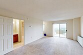 Located in Silver Spring, Maryland, this efficiently designed single-floor unit offers a thoughtful layout that maximizes every square foot. The open living area is anchored by soft, neutral carpeting and bright white walls, creating a clean and airy atmosphere. A sliding glass door leads to a private balcony, allowing natural light to fill the space while offering views of the surrounding area.

The kitchen is positioned adjacent to the living area and features warm wood cabinetry with stone-toned countertops and a white refrigerator, providing functional storage and prep space. A dedicated closet offers additional storage, thoughtfully integrated into the floor plan.

The unit includes two bathrooms. The primary bathroom is finished with large-format marble-style tile lining the walls of a full soaking tub and shower combination, paired with light tile flooring for a clean, polished look. The second bathroom features a warm wood vanity with a white countertop, a mirrored medicine cabinet, and tile flooring, offering a practical and well-appointed space.

Throughout the unit, the neutral color palette and consistent finishes create a cohesive, move-in-ready environment. A welcoming entryway completes the layout, making this a well-organized and functional space in a convenient Silver Spring location.