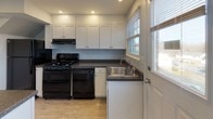 This two-story, 2-bedroom, 2-bathroom home offers a clean and functional layout across two well-organized floors. The main level features an open living area with light gray walls and durable light-toned hardwood-style flooring that reflects abundant natural light streaming in through multiple windows. A white staircase with classic railings connects to the upper level, and a built-in storage closet beneath the stairs maximizes utility. The kitchen is well-appointed with white shaker-style cabinetry, dark countertops, black appliances including a gas range and dishwasher, a stainless steel sink, and recessed lighting overhead. Multiple windows in the kitchen provide natural light and outdoor views. The main-level bathroom features large-format tile flooring, a white vanity, and a full tub-shower combination. Upstairs, two generously sized bedrooms are finished with plush wall-to-wall carpeting and soft neutral paint. Each bedroom includes windows with outdoor views and individual wall-mounted HVAC units for climate control. One bedroom features a closet with built-in rod storage. The second full bathroom on this level showcases white subway tile wainscoting, a window for natural light and ventilation, and a clean, minimalist vanity. The home presents a fresh, move-in-ready aesthetic throughout.