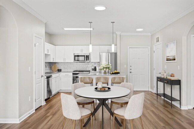 Comedor con cocina abierta, isla con asientos y acabados luminosos que crean un ambiente acogedor para las comidas compartidas y la vida cotidiana. - The Avens at Dedham Station