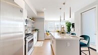 This well-designed 1-bedroom, 1-bathroom unit offers a thoughtful, efficient layout across a single floor. The open-concept kitchen and living area forms the heart of the space, bathed in natural light from multiple large windows fitted with blinds. The kitchen is outfitted with stainless steel appliances — including a gas range, microwave, dishwasher, and a full-size refrigerator — complemented by white cabinetry, open shelving, a subway tile backsplash, and a central island with a quartz countertop that provides additional seating and prep space. Sleek pendant lighting hangs above the island, adding a modern touch. The adjoining living room is generously lit with windows on two walls, creating a bright and airy ambiance, and features a ceiling fan for year-round comfort. Light hardwood-style flooring flows seamlessly through the main living areas. A hallway with closet storage connects the living areas to the private bedroom, which features plush carpeting, two large windows, and ample natural light. The full bathroom is finished with wood-look tile flooring, a glass-enclosed shower, and a white vanity. The overall aesthetic is clean, contemporary, and cohesive throughout.