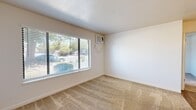 Located at 710 Wimbledon Drive in Lodi, California, this single-story, one-bedroom, one-bathroom unit offers a practical and efficiently designed layout across a compact footprint. The floor plan connects a living area, bedroom, kitchen, and bathroom in a straightforward arrangement well-suited for single occupancy.

The living area features neutral-toned carpeting, white textured ceilings, and a large picture window fitted with horizontal blinds that allows natural light to filter in while providing views of the surrounding greenery. A wall-mounted air conditioning unit provides climate control. The bedroom mirrors this aesthetic with matching carpet and another generously sized window offering outdoor views, maintaining a bright and neutral atmosphere throughout.

The galley-style kitchen is a functional highlight, featuring warm honey-toned wood cabinetry on both sides, light countertops, wood-look vinyl flooring, and white appliances including a range and refrigerator. A window above the counter adds natural light to the space. Mirrored panels near the kitchen entry contribute a sense of added depth.

The bathroom is clean and simply appointed, with a full tiled tub-shower surround, wood-look flooring, and a wood-framed vanity. Overall, the unit maintains a consistent, understated aesthetic throughout.