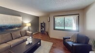 Located at 212 Park Meadows Dr in Waite Park, Minnesota, this single-floor residence offers a thoughtfully designed layout with a cohesive blend of functional spaces and comfortable finishes. The living room serves as a welcoming centerpiece, featuring rich wood-style flooring, a bold accent wall in deep gray, a textured ceiling, and a large window that invites natural light and outdoor views. A baseboard heating system runs along the perimeter, complementing the room's warm ambiance.

Adjacent to the living area, a dedicated dining space accommodates a full table setting beneath a contemporary chandelier, with wood-style flooring continuing the visual flow from the living room. The galley-style kitchen is well-equipped, showcasing dark wood cabinetry, a mosaic tile backsplash, light countertops, and white appliances, including a refrigerator and dishwasher. A double-door closet at the end of the kitchen provides generous storage.

The bedroom offers plush carpeting, a textured ceiling, and windows that allow natural light to filter in. The bathroom features tile flooring, a soaking tub with shower, and a vanity with dark cabinetry. A standout feature is the walk-in closet accessible from the bathroom, complete with built-in shelving for ample organization. An additional carpeted flex space provides versatility for various uses.
