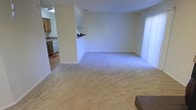 This two-floor space features an open-concept main level where the living area and kitchen flow seamlessly together. The living area is finished with wall-to-wall beige carpeting, contributing to a warm, neutral atmosphere throughout. Cream-painted walls provide a clean, understated backdrop that maximizes the sense of openness.

The kitchen is positioned to the side and is partially separated by a half-wall partition, creating a defined yet connected space. It features light wood cabinetry, a white dishwasher, and a hard-surface floor that contrasts with the carpeted living area. A range hood is visible above the cooking area, and the kitchen benefits from its own overhead lighting.

Natural light enters the living area through a large window, brightening the space and enhancing the airy feel. The open layout between the kitchen and living area makes the main floor well-suited for both everyday living and entertaining. The overall design is straightforward and functional, with neutral finishes that offer flexibility for various interior styles. The second floor adds additional living space beyond the main level.