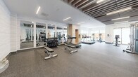 Located at 150 Wissler Rd in Waterloo, Ontario, this fitness facility offers a thoughtfully designed exercise room that provides a comprehensive workout environment. The space features a striking ceiling design with dark wood beam accents set against a white backdrop, complemented by recessed linear lighting that creates a bright and energizing atmosphere.

The exercise room is generously proportioned and outfitted with a full range of fitness equipment, including multiple treadmills, elliptical trainers, stationary bikes, and a Matrix cable machine system. A dedicated free weights area includes a dumbbell rack paired with adjustable benches, with floor-to-ceiling mirrors lining one wall to enhance the sense of space and support proper form during training.

Large windows along the exterior wall flood the space with natural light and offer views of the outdoor greenery, creating an inviting workout environment. The durable rubberized flooring throughout provides comfort and safety for all types of exercise. A built-in light wood storage unit adds a functional and aesthetic touch near the cardio zone. A water fountain station is also available within the space. The clean, contemporary finishes and open layout make this facility a well-rounded and accessible fitness destination.
