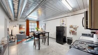 Located at 369 E Gay St in the heart of Columbus, Ohio, this two-bedroom, one-bathroom loft-style unit offers a distinctive urban living experience defined by its industrial architectural character. Exposed metal ceilings with visible ductwork and structural beams run throughout the space, giving it a raw, warehouse-inspired aesthetic that is both modern and functional.

The open living area serves as the heart of the unit, featuring polished concrete floors, large windows that invite natural light, and bold orange curtains that add a warm pop of color. The kitchen is outfitted with light wood cabinetry set against a vibrant orange accent wall, dark countertops, and black appliances including a full-size refrigerator, electric range, and microwave — offering a practical and visually striking cooking space.

Both bedrooms feature soft carpet flooring and are accented with artistic wall murals that bring energy and personality to each room. One bedroom benefits from a large window with sheer curtains, providing natural light and outdoor views. The shared full bathroom includes a single-sink vanity with wood cabinetry, dark countertops, a walk-in shower, and a large mirror — clean and efficiently laid out. This unit combines creative design with urban convenience in a compact, single-floor layout.