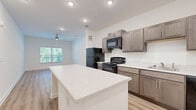 Located at 4029 Flat Shoals Pkwy in Decatur, GA, this well-appointed one-bedroom, one-bathroom unit offers a thoughtfully designed single-floor layout. The open-concept kitchen and living area serves as the heart of the home, featuring light wood-style flooring, recessed lighting, and a ceiling fan. The kitchen is outfitted with taupe shaker-style cabinetry, light quartz countertops, a central island, and a full suite of black appliances including a refrigerator, gas range, over-the-range microwave, and dishwasher. Natural light flows in through a window overlooking lush greenery, creating an airy and welcoming atmosphere. The bedroom is carpeted for comfort and includes a ceiling fan, a window with outdoor views, and direct access to a spacious walk-in closet equipped with multi-level wire shelving for ample storage. The bathroom continues the home's modern aesthetic with wood-style flooring, a framed vanity mirror, taupe cabinetry with a light countertop, and clean white walls. Throughout the unit, crisp white walls and consistent finishes create a bright, cohesive, and move-in-ready environment.