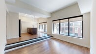Located at 156 S Main St in the heart of downtown Akron, Ohio, this single-floor unit offers a thoughtfully designed open-concept layout with contemporary finishes throughout. The living area features warm hardwood-style flooring and expansive floor-to-ceiling windows framed in dark trim, flooding the space with natural light while offering direct views of the surrounding urban streetscape.

A distinctive raised platform separates the kitchen from the main living area, adding architectural interest and definition to the open floor plan. The kitchen is well-appointed with dark espresso cabinetry, a long quartz-topped island with an undermount sink, stainless steel appliances including a refrigerator, range, and microwave, a tile backsplash, and pendant lighting overhead. Additional workspace and storage are provided by upper and lower cabinetry along the back wall.

The bedroom is carpeted for comfort and features a large multi-pane window with city views, elevated ceilings, and access to a generously sized walk-in closet with built-in shelving. The bathroom is finished with large-format tile, a sliding glass-door walk-in shower, a dark wood vanity with a light-topped mirror, and recessed lighting, delivering a clean and modern aesthetic throughout.