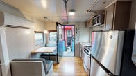 This one-of-a-kind unit at Germantown Mill Lofts is housed within a converted train car, offering a distinctive living experience that preserves the vehicle's original structural character while incorporating modern interior updates. The elongated, single-floor layout follows the natural form of the rail car, with warm hardwood floors running the full length of the space and contributing a sense of continuity throughout.

The kitchen is efficiently designed, featuring stainless steel appliances including a refrigerator, electric range, microwave, and a single-basin sink set into a wood-toned countertop. Cabinetry above and below provides functional storage, and a small window above the sink brings in natural light. Adjacent to the kitchen, a cozy dining nook features built-in booth-style seating in gray upholstery arranged around a compact table, with windows offering views of the surrounding environment.

The corridor-style hallway connects the various sections of the space, with exposed conduit running along the ceiling — a nod to the industrial origins of the structure. Separate enclosed rooms branch off the main corridor, offering defined private areas. The open end room, featuring a door with a window, provides additional flexible space. A wall-mounted mini-split unit handles climate control throughout.