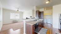 This thoughtfully designed 2-bedroom, 2-bathroom residence offers a practical and comfortable single-floor layout. The open-concept kitchen and dining area serves as the heart of the home, showcasing rich dark wood cabinetry, granite countertops, and a peninsula breakfast bar that provides additional counter space and seating. Black appliances, including a refrigerator and electric range, complement the kitchen's modern aesthetic, while rich hardwood-style flooring extends throughout the main living areas. An in-unit washer and dryer are conveniently located just off the kitchen. The living area features a ceiling fan and a window that brings in natural light. A hallway connects the two bedrooms, each carpeted for added comfort and equipped with windows that frame outdoor greenery. The primary bedroom offers a generous footprint and direct access to a closet. Both bathrooms are finished with granite-topped vanities, dark wood cabinetry, and stylish hexagonal tile flooring, with at least one bathroom featuring a walk-in shower. Neutral wall tones and consistent finishes throughout lend the space a clean, cohesive feel, making it a functional and inviting place to call home.