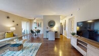 Located at 1691 Mesa Dr in Newport Beach, California, this single-floor residence offers a thoughtfully designed layout that balances comfort and functionality. Rich hardwood-style flooring flows throughout the main living areas, anchoring an open-concept floor plan that seamlessly connects the living room, dining area, and kitchen.

The living room is generously proportioned, featuring a textured ceiling, bold wall art, and a glass coffee table set atop a vibrant area rug. A large flat-screen TV and media console complete the space. The dining area is positioned near sliding glass doors that open to a private patio, filling the space with natural light and outdoor views of lush greenery.

The kitchen is well-appointed with white shaker cabinetry, granite-style countertops, stainless steel appliances including a refrigerator and dishwasher, and recessed lighting. A ceiling fan overhead adds to the room's practicality.

Two bedrooms offer carpeted flooring, vertical blinds, windows with verdant views, and ample closet space — the primary bedroom features mirrored sliding closet doors. The two bathrooms include one with a walk-in glass-enclosed shower and another with a full tub-shower combination and granite vanity countertop. The textured ceilings and neutral wall tones throughout provide a cohesive, welcoming ambiance.