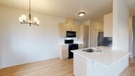This single-floor residence is designed with a clean, contemporary aesthetic throughout. The kitchen serves as a central feature, equipped with light wood-tone cabinetry extending to the ceiling for ample storage, white countertops, and a full suite of black appliances including a range, over-the-range microwave, and refrigerator. A peninsula with an integrated sink provides additional workspace and adds an open, functional layout that connects seamlessly to the living and dining areas. A stylish chandelier anchors the dining space nearby.

The living area benefits from multiple windows that invite generous natural light and frame outdoor views of the surrounding landscape. A wall-mounted PTAC unit provides climate control, and a door leads directly to an outdoor balcony. Vaulted ceiling lines and a ceiling fan enhance the sense of openness in this space.

The bedrooms are well-proportioned, each featuring large windows that continue the theme of natural light and outdoor views. Light hardwood-style flooring runs consistently throughout the unit, contributing to a cohesive, modern feel.

The bathroom is a standout space, featuring a distinctive patterned tile floor with an intricate geometric design that adds visual character. A vanity with matching wood-tone cabinetry, a grab bar, and a small window complete the room's practical and thoughtful design.