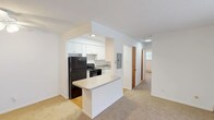 This single-floor residence offers a practical and comfortable layout designed for everyday living. The kitchen is a standout feature, showcasing crisp white cabinetry, granite-style countertops, hardwood flooring, and black appliances including a refrigerator, range, and dishwasher. A peninsula counter opens seamlessly to the adjacent living area, creating an ideal flow for daily life and entertaining. The living room is generously proportioned, filled with natural light from a large sliding glass door fitted with vertical blinds, and includes a wall-mounted air conditioning unit and baseboard heating for year-round comfort. Soft carpet extends throughout the living and bedroom areas, adding warmth underfoot. Ceiling fans with integrated lighting are found in both the living room and bedrooms, enhancing comfort and air circulation. The bedrooms are well-sized, with clean white walls, carpeted floors, and natural light from windows overlooking greenery. Warm wood-toned interior doors add a classic touch throughout the unit. The bathroom features a full soaking tub and shower combination with a distinctive blue mosaic tile surround, complemented by neutral tile flooring. A hallway connects the main living spaces to the bedrooms and bathroom, with convenient closet access along the way.