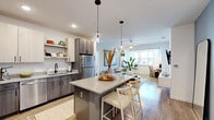 This single-floor residence offers a thoughtfully designed open-concept layout that maximizes its comfortable footprint across two bedrooms, two bathrooms, and dedicated living and kitchen areas. Light wood-tone flooring flows consistently throughout, creating a cohesive and airy aesthetic.

The kitchen serves as a central hub, featuring two-tone cabinetry pairing white upper cabinets with warm gray lower units, granite countertops, and stainless steel appliances. A granite-topped island with seating anchors the space, illuminated by glass pendant lights. Open shelving adds additional storage and display space.

The living area connects seamlessly to the kitchen and extends into a naturally lit flex nook framed by a large window with outdoor views, ideal as a reading corner or workspace. The primary bedroom includes its own closet and connects to a full bathroom with a walk-in glass-enclosed shower and granite vanity. The second bedroom features natural light and a ceiling fan. The second bathroom includes a granite vanity and wood-look flooring. Both bathrooms maintain consistent modern finishes throughout. Each bedroom includes closet storage, contributing to the overall functionality of this well-appointed residence.