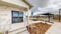 Located at 16601 East Braker Lane in Austin, Texas, this single-story facility is designed with both functionality and accessibility in mind. The exterior showcases a durable combination of natural limestone and lap siding, giving the building a clean, modern aesthetic that blends well with its surroundings.

The entrance area is thoughtfully designed to accommodate all visitors, featuring both stepped access and a dedicated ADA-compliant ramp with handrails, alongside reserved accessible parking spaces. Double glass doors with dark frames provide a welcoming entry point, while a covered overhang offers protection from the elements.

The property encompasses a generously sized open outdoor yard enclosed by a sturdy wire-panel fence, ideal for recreational use. Several young trees have been planted throughout the grounds, contributing to the developing landscape. Exterior lighting poles are positioned throughout the outdoor area to ensure visibility after dark.

A covered pavilion or shade structure is visible toward one end of the property, offering a sheltered outdoor gathering space. Utility infrastructure, including waste management enclosures, is neatly tucked within the grounds. The paved parking area is well-marked and accessible, supporting smooth traffic flow for visitors and staff.

The surrounding landscape opens up to natural wooded views beyond the fence line, providing a sense of openness and connection to the natural environment of the Austin Hill Country region.