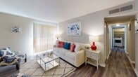 Located at 100 Turtle Creek Dr in Greenville, South Carolina, this single-floor residence offers a well-organized layout designed for comfortable everyday living. The galley-style kitchen is outfitted with crisp white cabinetry, dark granite-look countertops, and stainless steel appliances including a refrigerator, electric range, and built-in microwave. Wood-look plank flooring runs throughout the main living areas, lending a cohesive and modern aesthetic. Adjacent to the kitchen, the dining area features a pass-through counter and is illuminated by a brushed nickel chandelier, creating an inviting space for meals and entertaining. The living room is generously proportioned, with a large sliding glass door dressed in vertical blinds that allows natural light to fill the space. Two bedrooms provide comfortable retreats, each finished with plush wall-to-wall carpeting and textured ceilings. Both rooms include closet storage, with one bedroom featuring a wide bi-fold closet and windows offering natural light. A bathroom with wood-look flooring connects to a hallway that flows through the unit. Neutral warm-toned walls throughout lend a calm, move-in-ready atmosphere to this well-appointed Greenville residence.