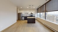 Located in the heart of Toledo, Ohio, this modern single-floor unit sits within a high-rise building on N St Clair Street, offering an impressive blend of contemporary finishes and elevated urban living. The open-concept living and kitchen area is anchored by light hardwood-style flooring and floor-to-ceiling windows fitted with sleek roller shades, providing sweeping panoramic views of the Toledo skyline and surrounding cityscape. The kitchen is well-appointed with dark espresso cabinetry contrasted by crisp white upper cabinets, granite countertops, a central island with pendant lighting, and a full suite of stainless steel appliances including a refrigerator, electric range, microwave, and dishwasher. The carpeted bedrooms offer a quiet retreat, each featuring generous closet space with sliding doors and dark-trimmed door frames that carry throughout the unit's interior design. The hallway connects the living spaces efficiently, with warm wood-tone flooring extending from the kitchen into the corridor. The bathrooms are clean and functional, each featuring a tub/shower combination, a dark-vanity with a large mirror, tile-style flooring, and brushed nickel fixtures. Throughout the unit, a neutral color palette, modern door hardware, and large-scale windows create a bright, cohesive, and polished atmosphere.