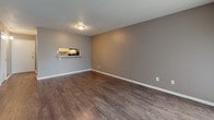 This single-floor residential unit offers a practical and well-appointed layout designed for comfortable everyday living. The living area is spacious and open, featuring dark hardwood-style flooring, neutral gray walls, and a textured ceiling. Natural light filters in through blinded windows, and a sliding glass door provides additional brightness and access to the outdoors. A pass-through window connects the living space to the kitchen, enhancing the open feel between the two areas.

The galley-style kitchen is efficiently designed with white cabinetry lining both sides, light-toned countertops, dark hardwood-style flooring, and black appliances including a range and refrigerator. Ample cabinet and counter space make this kitchen highly functional.

The bedrooms are carpeted in a warm neutral tone and feature gray walls with textured ceilings. The primary bedroom includes a generous double closet alongside an additional door, offering plentiful storage. A second bedroom provides a quiet, versatile space suitable for various uses.

The bathroom is clean and straightforward, featuring a full tub-shower combination with white subway tile surround, chrome fixtures, and a toilet. Throughout the unit, consistent neutral tones and practical finishes create a cohesive and move-in ready environment.