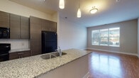 This single-floor residence at 23220 Chagrin Blvd in Beachwood, Ohio offers a well-designed, modern interior with a cohesive aesthetic throughout. The kitchen is a standout feature, showcasing dark espresso-toned cabinetry that extends floor to ceiling, granite countertops, a tile backsplash, and black appliances including a refrigerator, range, and microwave. A peninsula with an integrated sink and pendant lighting above creates a natural transition into the open living and dining area, which features warm hardwood flooring and a large window that fills the space with natural light and outdoor views. The hallway connects the main living area to the private rooms, maintaining the hardwood flooring and a clean, open feel. The bedrooms are carpeted for comfort, each offering neutral tones and windows that bring in additional natural light. The bathroom is appointed with a dark wood vanity, granite countertop, a large framed mirror, and large-format tile flooring. An adjacent walk-in closet provides generous storage. The overall ambiance is contemporary and refined, with consistent use of dark wood, granite surfaces, and warm flooring creating a cohesive and inviting living environment.