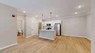 This thoughtfully designed 1-bedroom, 1-bathroom unit offers a functional and modern living experience across a single floor. The open-concept layout seamlessly connects the kitchen, dining, and living areas, creating a bright and cohesive space. The kitchen is a standout feature, showcasing white shaker cabinetry, a classic subway tile backsplash, granite countertops, and a large center island with a built-in sink and pendant lighting overhead. Stainless steel appliances, including a refrigerator, microwave, and range, complete the kitchen. Light hardwood flooring flows throughout the main living areas, complemented by neutral-toned walls and crown molding that add a refined architectural detail. The living room benefits from natural light through large windows fitted with blinds, and features a ceiling fan for added comfort. The bedroom is carpeted, offering a cozy retreat with ample natural light from a window. The full bathroom includes a white vanity with granite countertops, a mirror with overhead lighting, and a bathtub. A dedicated laundry room with overhead wire shelving and washer/dryer hookups adds everyday convenience. Recessed lighting throughout ensures a bright, welcoming ambiance across the entire unit.