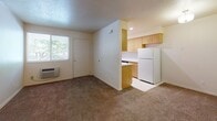 This single-floor unit offers a straightforward, functional layout designed for comfortable everyday living. The living area is generously sized, featuring warm beige carpet flooring, neutral white walls, and a textured ceiling. A large sliding glass door fitted with vertical blinds allows abundant natural light to fill the room while providing outdoor access. A wall-mounted HVAC unit ensures climate control convenience.

The kitchen is positioned adjacent to the living area in a semi-open configuration. It features light wood cabinetry with brushed metal hardware, white laminate countertops, tile flooring, and a full suite of appliances including an electric coil stovetop, dishwasher, and refrigerator. A window above the sink brings in additional natural light and outdoor views.

The bedroom is well-proportioned with plush carpet flooring and white walls, offering a calm and neutral environment. It connects directly to the bathroom, which includes a full-size tub and shower combination, a wood-toned vanity with a white countertop, tile flooring, and a frosted window for natural light and privacy. A closet with bi-fold doors provides dedicated storage within the bedroom corridor.