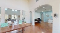 This single-floor community facility spans a generously sized footprint, offering a diverse range of functional spaces unified by a cohesive design aesthetic. The grand entry lobby immediately establishes the tone, featuring soaring ceilings, elegant arched doorways, polished concrete tile flooring, and a statement chandelier suspended above a rustic wooden table. Large windows and glass-paneled entry doors flood the space with natural light, creating a welcoming first impression.

Adjacent to the lobby, the lounge area serves as a comfortable gathering space highlighted by a dramatic floor-to-ceiling stone fireplace, slate-blue accent walls, and abundant natural light streaming through clerestory windows. A dining area nearby benefits from an oversized window with outdoor views and the same high ceilings that define much of the space.

The leasing office provides a professional, open workspace with recessed lighting, arched architectural details, and ample room for multiple workstations. A compact kitchen features dark marble-style countertops and gray cabinetry, offering practical utility.

The fitness center is bright and airy, showcasing a vaulted ceiling, a large arched window, and multiple cardio machines. A dedicated laundry room provides rows of washers and dryers, while a separate package locker room offers secure parcel storage with wood-look flooring.
