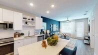 This single-floor residence offers a thoughtfully designed open-concept layout that seamlessly connects the kitchen, dining, and living areas. The kitchen is outfitted with sleek flat-front white cabinetry extending to the ceiling, stainless steel appliances including a range, microwave, dishwasher, and refrigerator, complemented by quartz countertops and open shelving. A generously sized kitchen island provides additional seating and prep space, while light wood-tone flooring flows throughout the main living areas. The living room makes a bold statement with a deep teal accent wall adorned with framed artwork, large windows that invite natural light, a ceiling fan, and a private exterior door. The bedroom is a calm retreat, featuring neutral toned walls, a ceiling fan, plush carpeting, and a large window that fills the room with light. The bathroom is well-appointed with a wide quartz vanity, an undermount sink, a large framed mirror, a soaking tub with white subway tile surround, and wood-look flooring. Recessed lighting throughout the space enhances the bright, modern aesthetic, creating a cohesive and comfortable living environment.