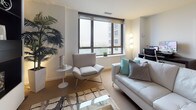 Located at 100 Parrott Dr in Shelton, Connecticut, this well-appointed single-floor residence combines modern design with functional living spaces. The open-concept living area is bright and inviting, featuring large floor-to-ceiling windows that flood the room with natural light and offer views of the surrounding cityscape. A sleek built-in entertainment wall with open shelving serves as a focal point, complemented by contemporary furnishings and a stylish patterned area rug over neutral carpeting. The kitchen is efficiently designed with warm wood cabinetry, stainless steel appliances including a range and built-in microwave, light tile flooring, and a breakfast bar that provides additional counter space. The primary bedroom is generously sized, showcasing expansive windows with outdoor views, soft carpeting, and a spacious walk-in closet with organized shelving and hanging storage. A second bedroom offers similar clean lines and natural light. The bathroom features tile flooring, a shower-tub combination, and a vanity with ample counter space. Throughout the residence, a consistent neutral color palette, clean architectural lines, and modern fixtures create a cohesive and contemporary ambiance ideal for comfortable urban living.