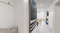 This thoughtfully designed single-floor residence combines contemporary finishes with a clean, modern aesthetic throughout. Light hardwood flooring flows seamlessly across the living spaces, complementing the crisp white walls and recessed lighting that give the interior a bright, airy feel.

The entryway, secured by a smart lock entry door, opens to a corridor adorned with a striking large-scale artwork, setting an elevated tone for the space. The living room is anchored by expansive floor-to-ceiling windows that frame urban views of the surrounding cityscape, flooding the room with natural light.

The kitchen is efficiently designed with white cabinetry, stainless steel appliances including a range and built-in microwave, and ample storage. A compact dining area with a dark wood table and benches sits adjacent, creating a cohesive and functional everyday living zone.

The primary bedroom benefits from large windows with urban views, built-in overhead cabinetry for generous storage, and light flooring that carries the home's unified palette. A second bedroom offers a quieter, well-appointed retreat with tasteful décor. The full bathroom features a floating vanity with an illuminated mirror, tiled flooring, and a combination tub and shower, reflecting the home's clean and modern design sensibility throughout.