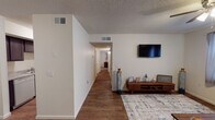 This single-floor residence offers a functional and comfortable layout with consistent wood-look flooring running throughout all areas. The living room serves as the heart of the home, featuring a ceiling fan with light fixture, large windows that allow natural light to fill the space, and a textured ceiling. A wall-mounted television area and open sightlines to the hallway give the space a connected feel.

The galley-style kitchen is outfitted with dark cabinetry, granite-look countertops, a double-basin sink, a white electric range, and a full-size refrigerator. A utility area is accessible directly from the kitchen, adding everyday convenience.

The primary bedroom is a standout space, offering room for a king-size bed, dual nightstands, and wall art. It includes a dedicated walk-in closet, a window for natural light, and a textured ceiling. A second bedroom provides a cozy and well-lit retreat with its own window. A third, smaller bedroom rounds out the sleeping quarters.

The bathroom features a single-sink vanity with a large mirror, a toilet, and a shower. A long hallway connects the private areas of the home to the main living spaces, enhancing the sense of separation between communal and personal areas. The overall ambiance is warm, neutral, and move-in ready.