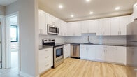 This thoughtfully designed single-floor residence offers a clean, contemporary aesthetic throughout. The primary kitchen is outfitted with crisp white shaker cabinetry, dark gray countertops, a white subway tile backsplash, and a full suite of stainless steel appliances including a range, over-the-range microwave, and dishwasher. Light hardwood flooring runs seamlessly underfoot, adding warmth to the modern palette. A secondary kitchen mirrors the same design language, featuring matching white cabinetry, gray countertops, a subway tile backsplash, and a stainless steel dishwasher paired with a brass-toned undermount sink and fixture.

The bathrooms are finished to a high standard. One features large-format warm stone floor tiles, marble-style wall tiles in the walk-in shower, and a white vanity with brass hardware. The second bathroom continues this refined approach with full marble-style tile surrounding a soaking tub, gray floor tiles, and matching brass fixtures throughout.

The living and bedroom spaces are bright and airy, finished in soft neutral tones with light hardwood flooring and recessed lighting. Large floor-to-ceiling windows frame expansive urban skyline views, filling each room with natural light and offering a compelling connection to the city below.