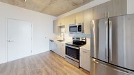 Located at 35 SW 6th Street in Miami's vibrant Brickell neighborhood, this modern urban unit showcases a compelling blend of industrial and contemporary design elements. The exposed concrete ceiling serves as a defining architectural feature throughout the space, lending an urban loft aesthetic that pairs seamlessly with the warm, wood-look luxury vinyl flooring found in every room.

The open-concept living area is bright and airy, anchored by floor-to-ceiling sliding glass doors that frame sweeping views of the Miami skyline and cityscape, flooding the space with natural light. A bold navy accent wall adds a striking contrast to the crisp white walls that define the rest of the unit.

The kitchen is well-appointed with light wood cabinetry, clean light-toned countertops, a stainless steel undermount sink, and a full suite of stainless steel appliances including a refrigerator, electric range, over-the-range microwave, and dishwasher. The layout is efficient and functional, flowing naturally into the main living area.

The bedroom features a closet with built-in shelving and rod, providing practical storage. The bathroom is finished with large-format neutral tile surrounding a soaking tub and shower combination, complemented by a light vanity with a stone-look countertop. Track lighting and recessed vents complete the thoughtfully designed interior.